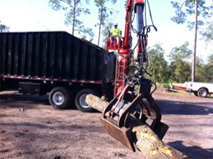 Tree removal crew member uses equipment to move log into truck - step 1